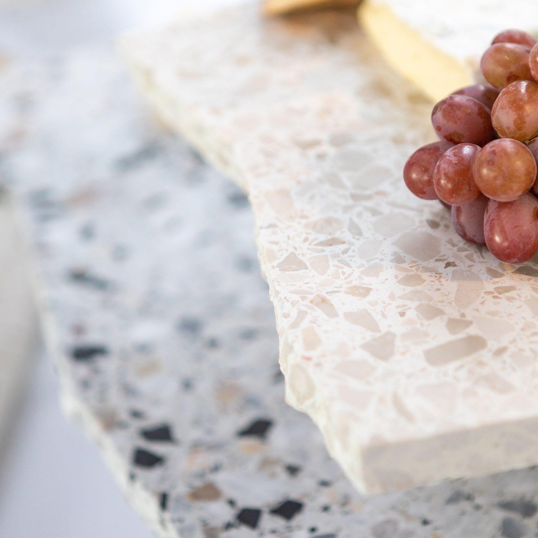 Detail shot of layered Insieme Homewares terrazzo platters — highlighting texture, craftsmanship, and the natural stone finish with fresh grapes.