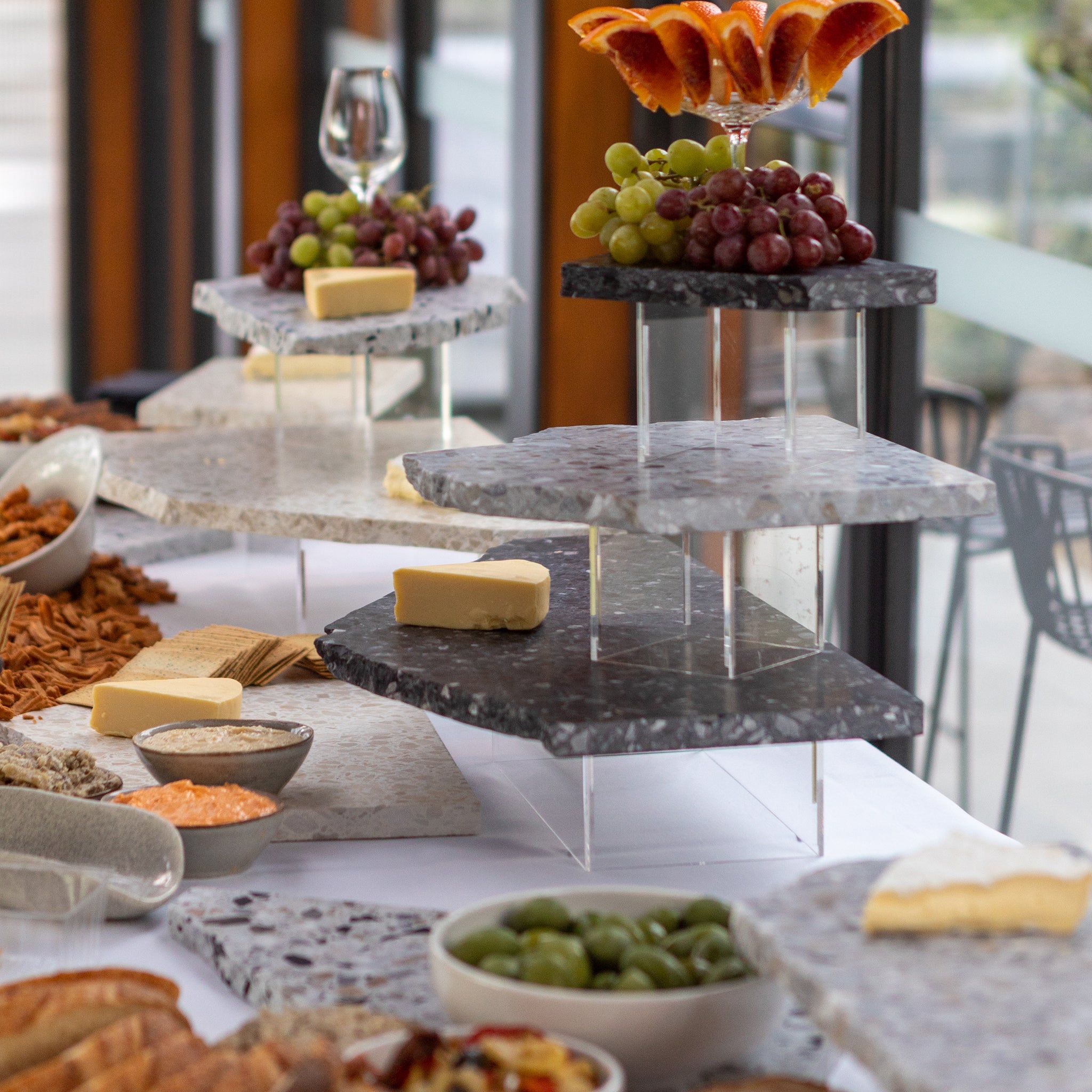 Insieme Homewares dark terrazzo platters styled with cheese, grapes, and antipasti — part of a modern grazing tower display at a catered event.