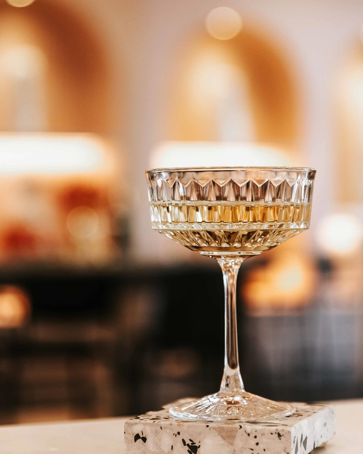 Crystal coupe glass placed on an Insieme Homewares terrazzo coaster — styled in a warm, ambient setting for elegant entertaining and elevated bar moments.