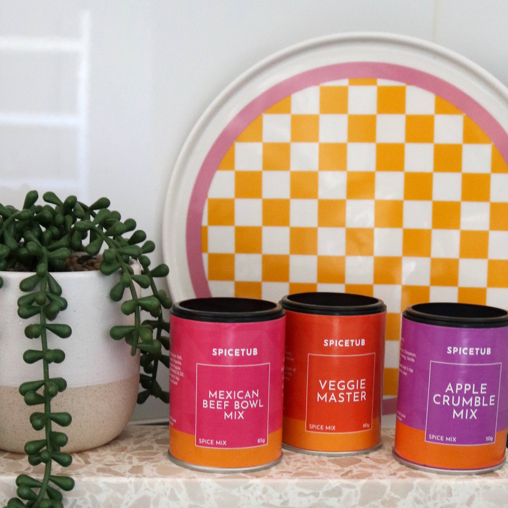 Trio of Spicetub spice blends arranged beside Insieme’s terrazzo platter and a vibrant checkered board, styled for a flavourful kitchen moment.