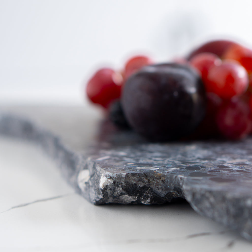 Side angle of an organic terrazzo platter in Inverno styled with red grapes and plums.
