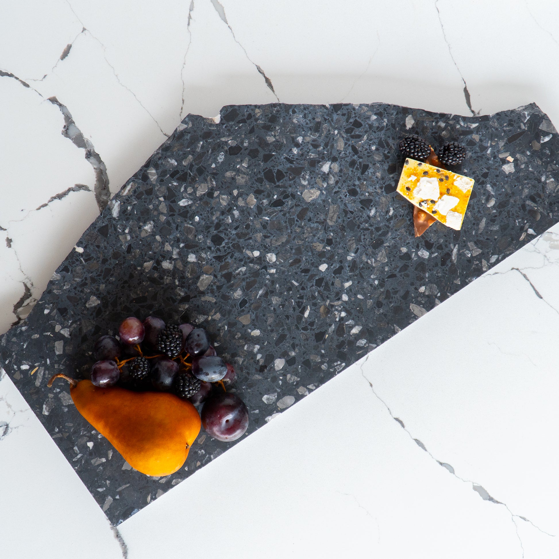 Flat lay of an Inverno organic terrazzo platter styled with chocolate bark and fruit.