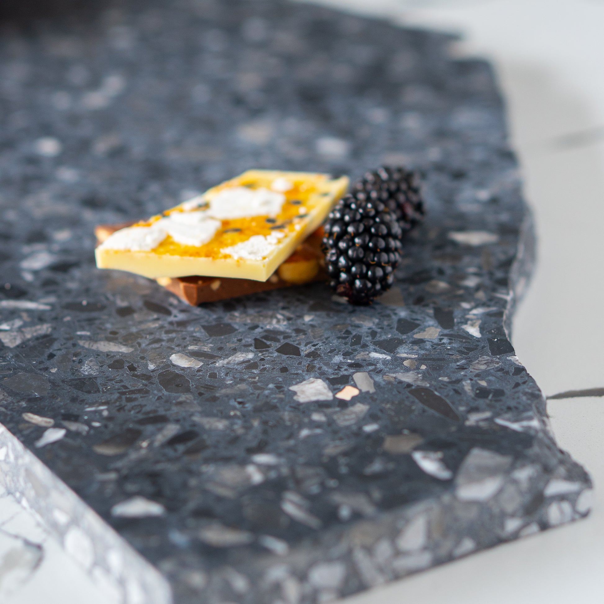 Close-up of chocolate bark and blackberries on an edge of an Inverno organic terrazzo platter.